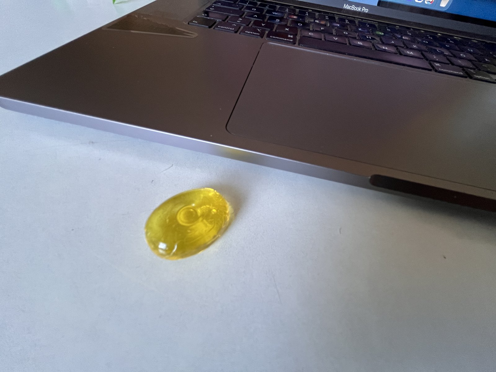 Ein gelbes Bonbon liegt auf einem weißen Tisch, direkt neben der Handballenauflage eines aufgeklappten MacBook Pro