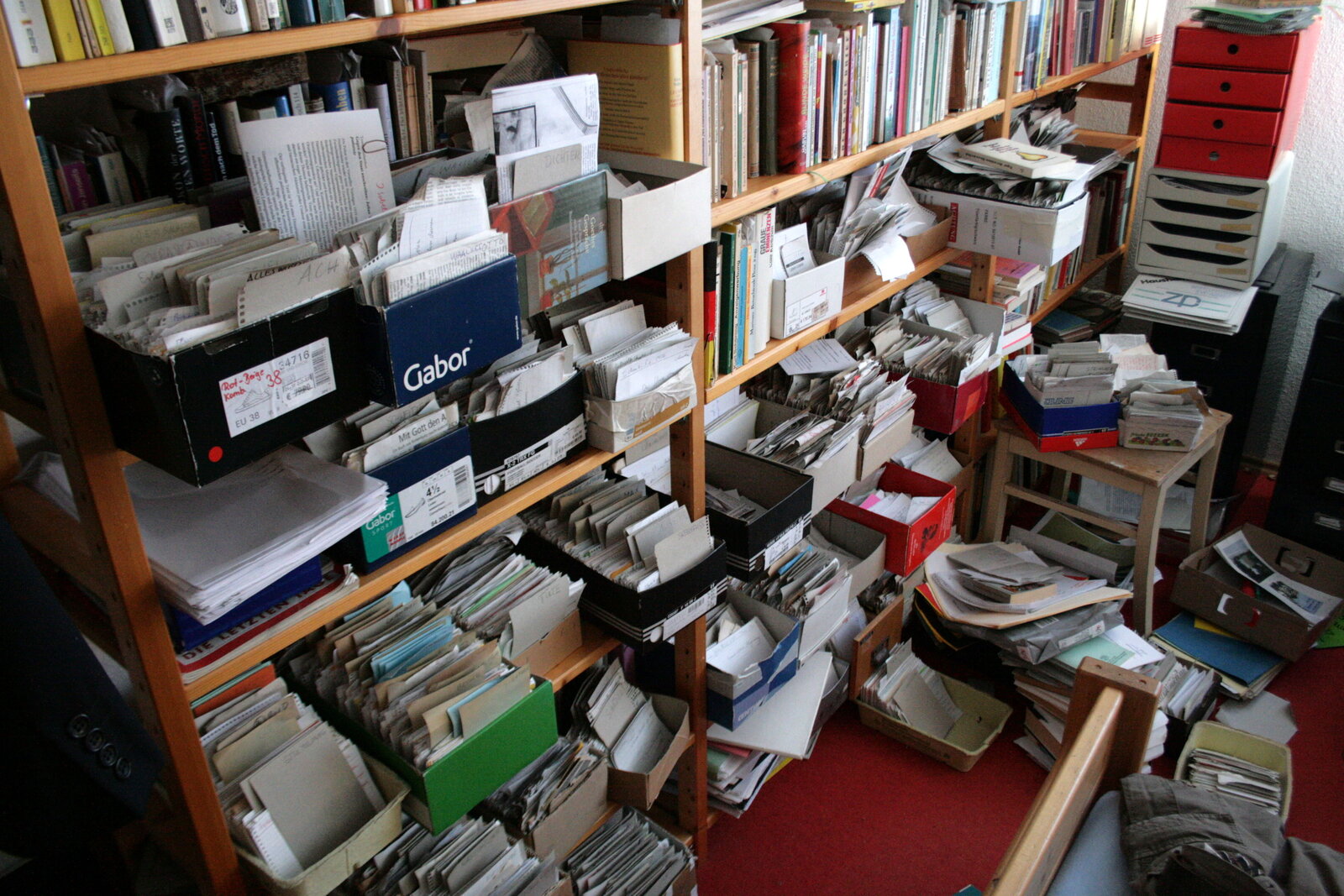 Regale voller Schuhkartons mit Zetteln, dazwischen Bücher